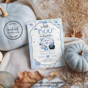 May include: A rectangular baby shower invitation card featuring a light blue and white watercolor background with a central ghost illustration, a black cauldron, and the text "a little BOO is almost due" in blue script and serif fonts.