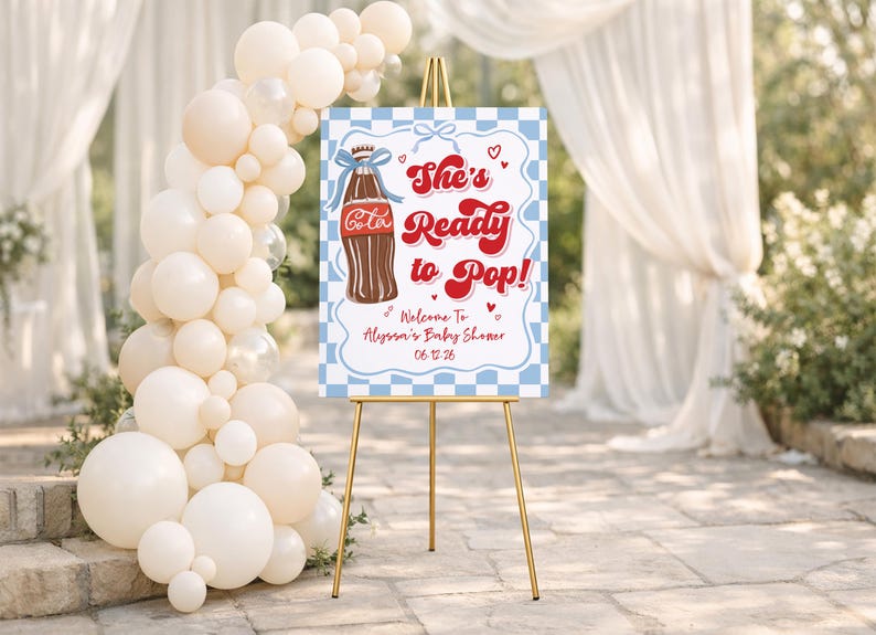 Puede incluir: Un letrero de bienvenida para baby shower sobre un caballete dorado. El letrero tiene un borde a cuadros azul y blanco y presenta una ilustraci&oacute;n de botella de cola y el texto "She's Ready to Pop!" con los detalles del baby shower.
