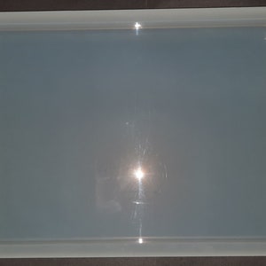 May include: A clear, rectangular resin tray with rounded corners. The tray is made of a smooth, translucent material and has a slight sheen.