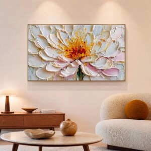 Könnte beinhalten: Ein rechteckiges Wandbild mit einem Ölgemälde einer großen, blühenden Blume mit dicken, strukturierten Impasto-Pinselstrichen. Die Blütenblätter sind hauptsächlich weiß und zartrosa, während die Mitte leuchtende Gelb- und Orangetöne zeigt.