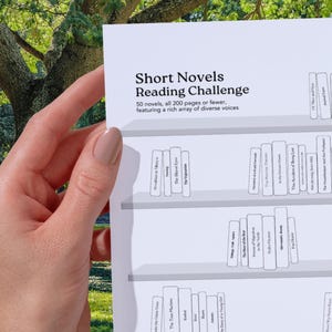 Könnte beinhalten: Ein weißes Papier mit dem Titel "Short Novels Reading Challenge" wird von einer Hand gehalten. Der Text lautet: "50 Romane, alle mit 200 Seiten oder weniger, mit einer reichen Vielfalt an Stimmen."
