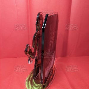 May include: A clear acrylic stand-up figure featuring a character with a head wrap and arm wraps. The figure is standing in front of a black rectangular panel. The base has green and yellow accents. The words "DEAN DRAWS" are printed on the stand.
