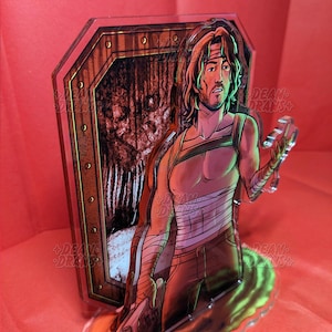 May include: A clear acrylic figure featuring a male character with long hair, a headband, and bandages. The figure is holding a chain and is in front of a wooden door design. The background is red.