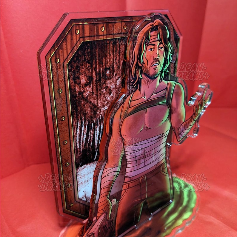 May include: A clear acrylic figure featuring a male character with long hair, a headband, and bandages. The figure is holding a chain and is in front of a wooden door design. The background is red.