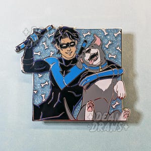 May include: Enamel pin featuring a character in a blue and black costume with a dog. The pin has a blue background with bone shapes. The character is smiling and holding two blue batons. The dog is gray and white.