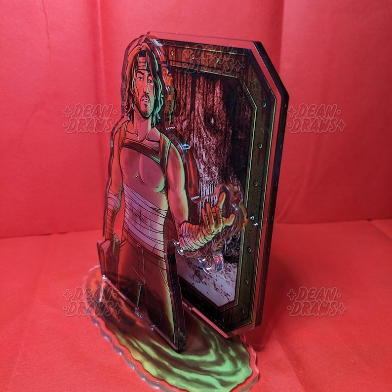 May include: A clear acrylic figure featuring a male character with long hair, bandages, and a sleeveless top. The figure is standing in front of a wooden door with a forest scene visible. The base is a green and yellow swirl.