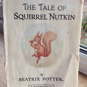 May include: A vintage book cover featuring a squirrel holding a nut. The title is "The Tale of Squirrel Nutkin" by Beatrix Potter. The book is published by F. Warne & Co. Ltd.