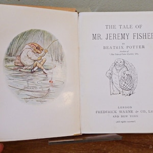 May include: An illustrated book open to two pages. The left page features a frog fishing scene. The right page displays the title "The Tale of Mr. Jeremy Fisher" by Beatrix Potter. Published by Frederick Warne & Co., London.