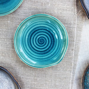 May include: Four ceramic plates in various shades of blue and gray. One plate features a swirling blue design.