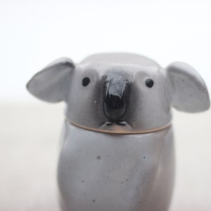 以下が含まれることがあります： グレーと白の斑点模様の釉薬が施されたセラミック製のユーカリのマグカップ。マグカップは黒い鼻と目があります。