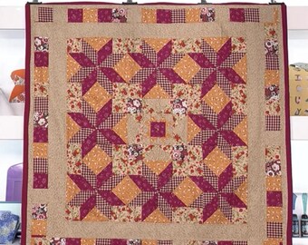 Könnte beinhalten: Ein quadratischer Quilt mit einem Sternmuster in Burgunder- und Orangetönen. Der Quilt hat einen Blumendruck und einen karierten Rand. Die Kanten sind mit einer dunkelroten Paspel versehen. Der Quilt wird auf weißem Hintergrund präsentiert.