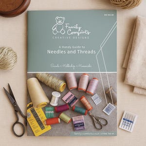 Puede incluir: Una vista superior de suministros de costura, incluyendo un libro titulado "A Handy Guide to Needles and Threads", carretes de hilo de varios colores, agujas y tijeras. La portada del libro presenta un logotipo de oso de peluche.