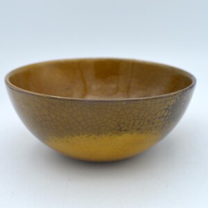 May include: A ceramic bowl with a crackle glaze. The base is golden yellow, transitioning to a darker, brownish-yellow at the rim. The crackle pattern gives the bowl a textured appearance.