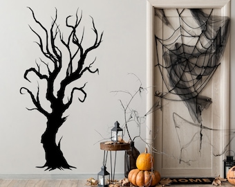 May include: A black wall decal of a leafless, twisted tree with gnarled branches. The tree is positioned next to a door covered in black spider web netting, with orange pumpkins, black lanterns, and dried leaves arranged on the floor.