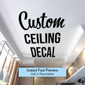 May include: Black text on a white ceiling reads "Custom CEILING DECAL" in a script and sans-serif font. A light blue banner below says "Instant Font Preview Link in Description". The image shows a modern interior with pendant lights.
