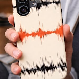 Könnte beinhalten: Eine Handyhülle mit cremefarbenem Hintergrund und einem Schallwellen-Design in Schwarz und Orange. Die Hülle hat eine Dual-Kamera-Anordnung und einen schwarzen Rand.