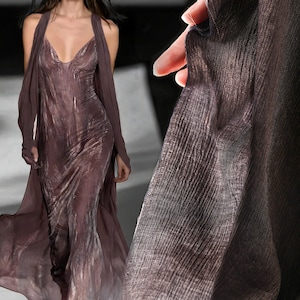 Könnte beinhalten: Ein fließendes, bodenlanges Kleid in einem gedämpften Malvenfarbton mit tiefem Ausschnitt und passendem, drapiertem Schal. Der Stoff scheint einen subtilen Glanz zu haben, wodurch ein luxuriöses Aussehen entsteht. Geeignet für formelle Anlässe.