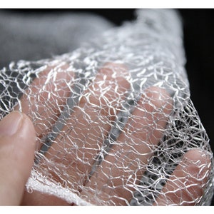 Pu&ograve; includere: Primo piano di un materiale sottile, bianco, traslucido e a rete. Il materiale &egrave; tenuto in una mano e sembra molto delicato.