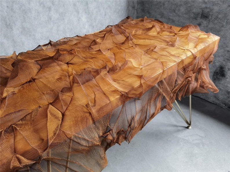 May include: A unique, sculptural table with a textured, layered surface in shades of brown and copper. The table has a rectangular top and is supported by thin, silver-colored legs. The design evokes a sense of organic forms and artistic craftsmanship.