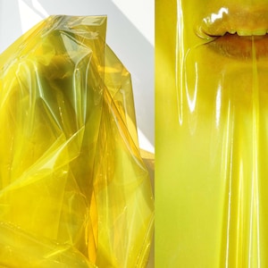 Pode incluir: Uma folha de plástico amarelo translúcido drapeada sobre uma superfície. O plástico é brilhante e tem um leve efeito de ondulação.