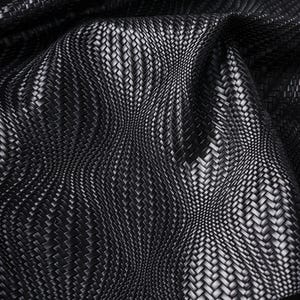 May include: Close-up of a black woven fabric with a textured basketweave pattern. The material has a subtle sheen, with light reflecting off the raised areas. The fabric is draped, creating soft curves and shadows.