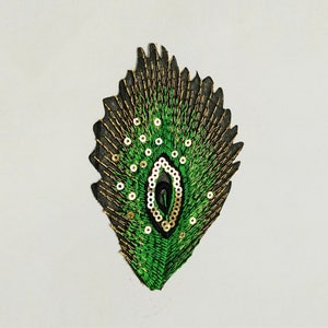 May include: A green and gold peacock feather embroidered patch with sequins. The patch is black and has a detailed design.