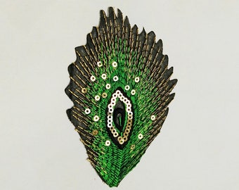 May include: A green and gold peacock feather embroidered patch with sequins. The patch is black and has a detailed design.