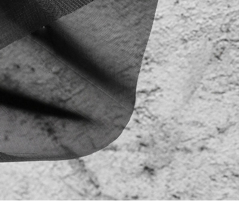 May include: Black sheer fabric with a fine mesh texture. The fabric is draped over a textured surface.