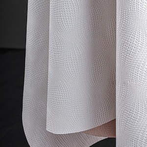 May include: Close-up of a textured, off-white fabric with a woven pattern. The fabric is draped, revealing folds and shadows. The material has a subtle, three-dimensional effect, creating a sense of depth and visual interest. The overall aesthetic is clean and modern.
