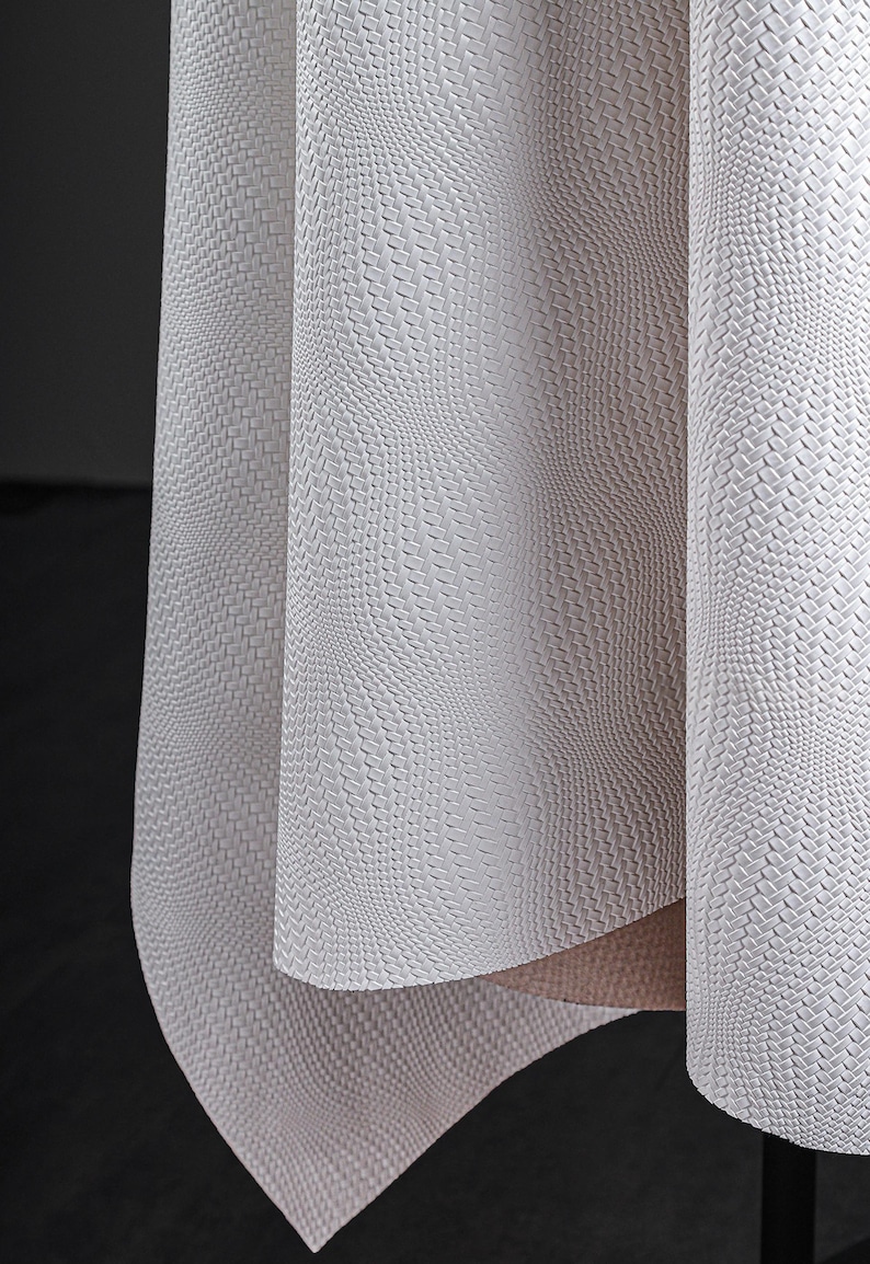 May include: Close-up of a textured, off-white fabric with a woven pattern. The fabric is draped, revealing folds and shadows. The material has a subtle, three-dimensional effect, creating a sense of depth and visual interest. The overall aesthetic is clean and modern.