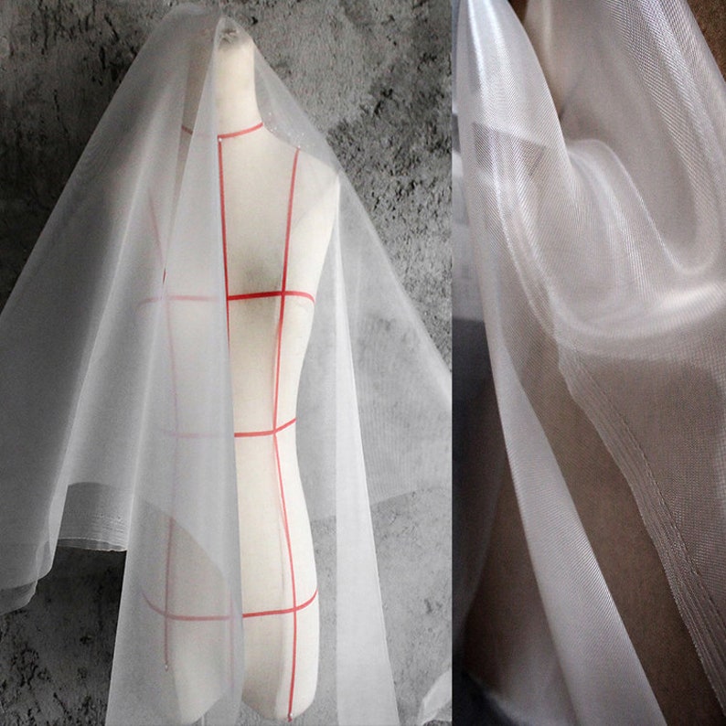 May include: White sheer tulle fabric with a fine mesh texture. The fabric is draped over a dress form and shown in a close-up.