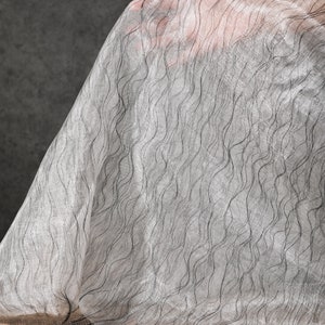 May include: A sheer white fabric with a wavy black pattern. The fabric is draped over a surface.