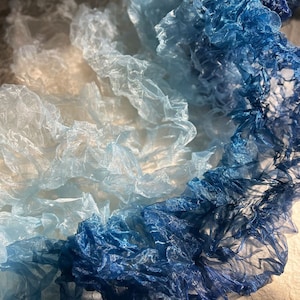 Puede incluir: Primer plano de una tela azul y blanca degradada con textura arrugada. La tela est&aacute; en capas y parece estar hecha de material transparente.