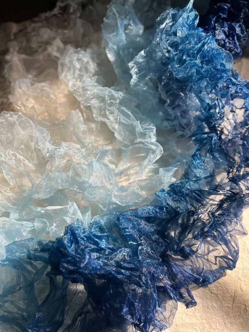Puede incluir: Primer plano de una tela azul y blanca degradada con textura arrugada. La tela est&aacute; en capas y parece estar hecha de material transparente.