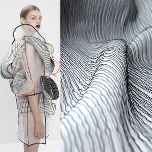May include: A white sheer fabric with black and orange lines. The fabric is draped and flowing, creating a wavy pattern.
