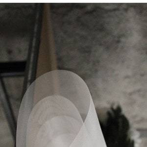 May include: A white, cylindrical, mesh lampshade with a slightly curved shape. The lampshade is made of a fine, woven material and has a subtle texture.
