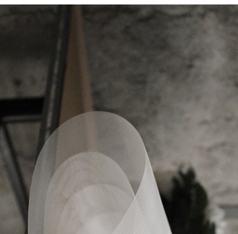 May include: A white, cylindrical, mesh lampshade with a slightly curved shape. The lampshade is made of a fine, woven material and has a subtle texture.