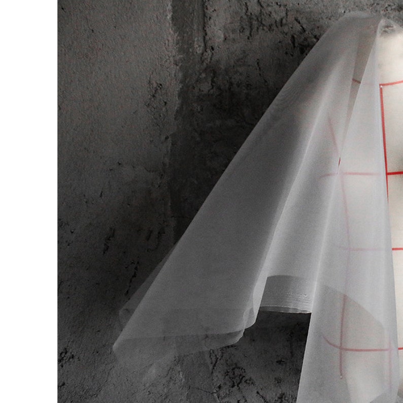 May include: A sheer white fabric draped over a textured gray surface. The fabric is translucent and has a slight sheen.