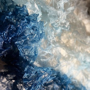 Puede incluir: Primer plano de una tela azul y blanca degradada con textura arrugada. La tela es transparente y delicada, con un suave y fluido drapeado.