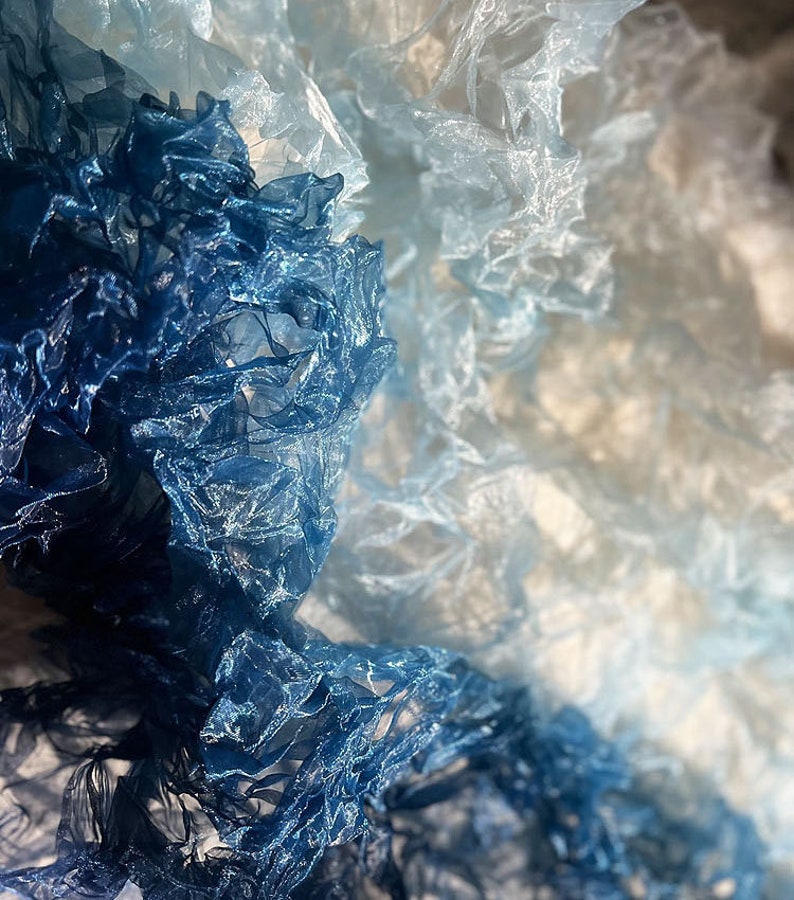 Puede incluir: Primer plano de una tela azul y blanca degradada con textura arrugada. La tela es transparente y delicada, con un suave y fluido drapeado.