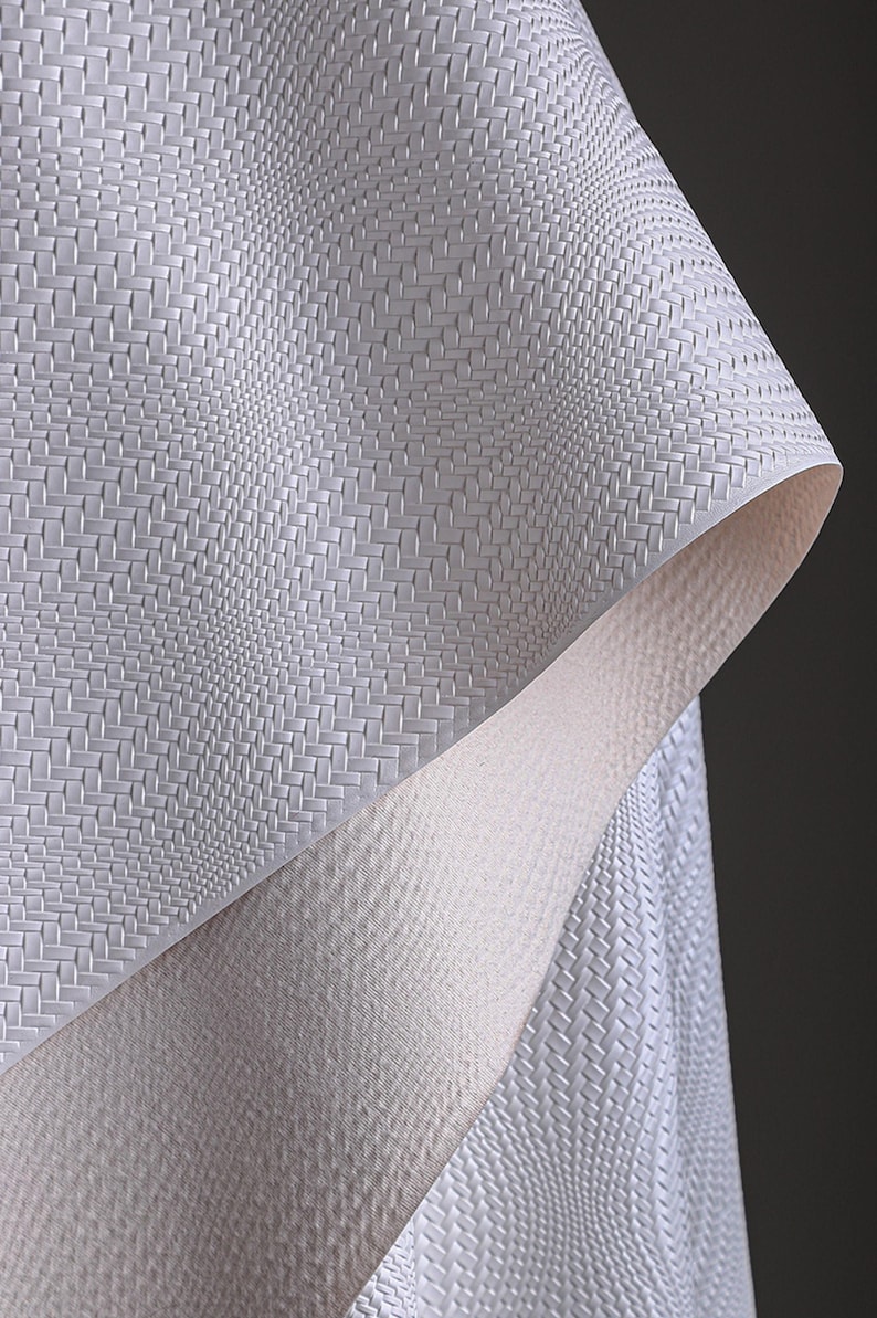 May include: Close-up of a textured, off-white material with a woven pattern. The material is folded, revealing a contrasting, smooth, light-coloured underside. The overall effect is a play of textures and tones.