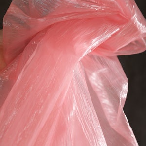 May include: Pink sheer fabric with a shimmery finish. The fabric is draped and folded, creating soft folds and wrinkles.