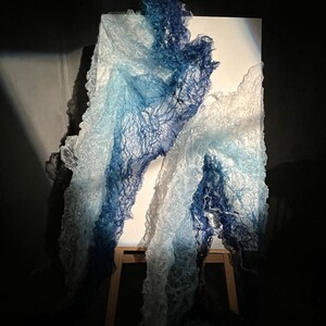 Puede incluir: Una escultura de tela azul y blanca sobre un caballete de madera. La tela est&aacute; drapeada y fluye, creando una sensaci&oacute;n de movimiento y fluidez.