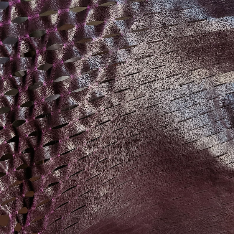 Puede incluir: Un material de color morado oscuro con una superficie texturizada y granulada que presenta un patr&oacute;n repetitivo de ranuras horizontales cortadas con l&aacute;ser. Los bordes de los cortes revelan una capa interior de color magenta brillante.