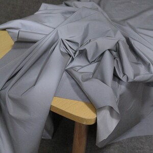 May include: A silver reflective fabric draped over a wooden table. The fabric is smooth and shiny, with a slight sheen.