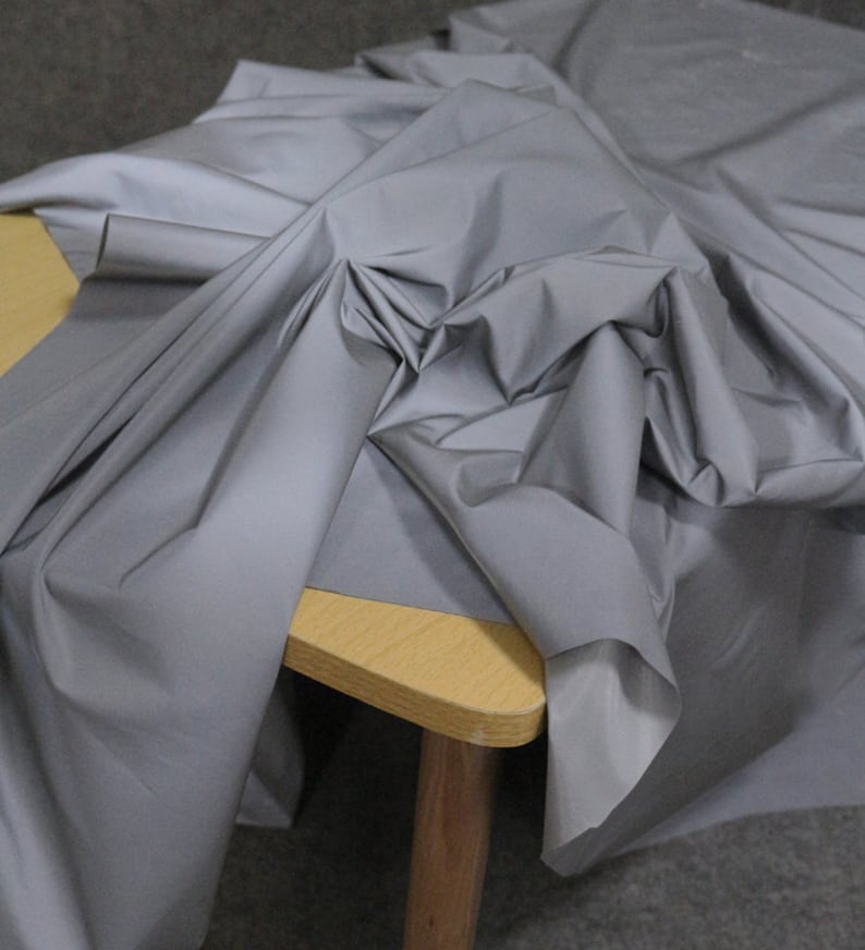 May include: A silver reflective fabric draped over a wooden table. The fabric is smooth and shiny, with a slight sheen.