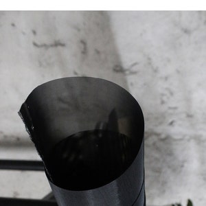May include: A black mesh fabric rolled up into a cylinder shape. The fabric has a fine weave and is slightly translucent.
