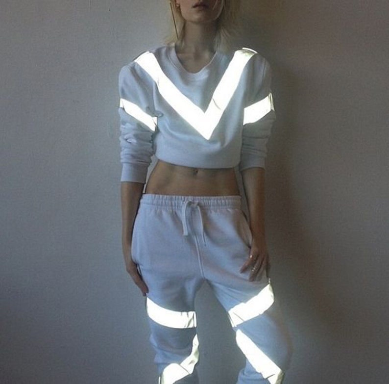 May include: White cropped sweatshirt with reflective chevron stripes and matching sweatpants with reflective stripes down the legs.