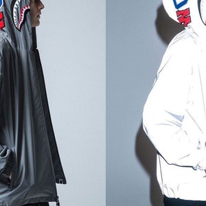 May include: Two hooded jackets, one gray and one white, with a shark graphic on the hood. Both jackets have a zipper closure and a drawstring at the waist.