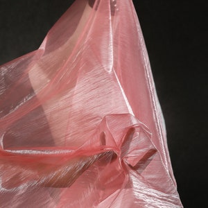 May include: A sheer pink fabric with a shimmery finish is draped and folded, creating a soft and flowing texture.